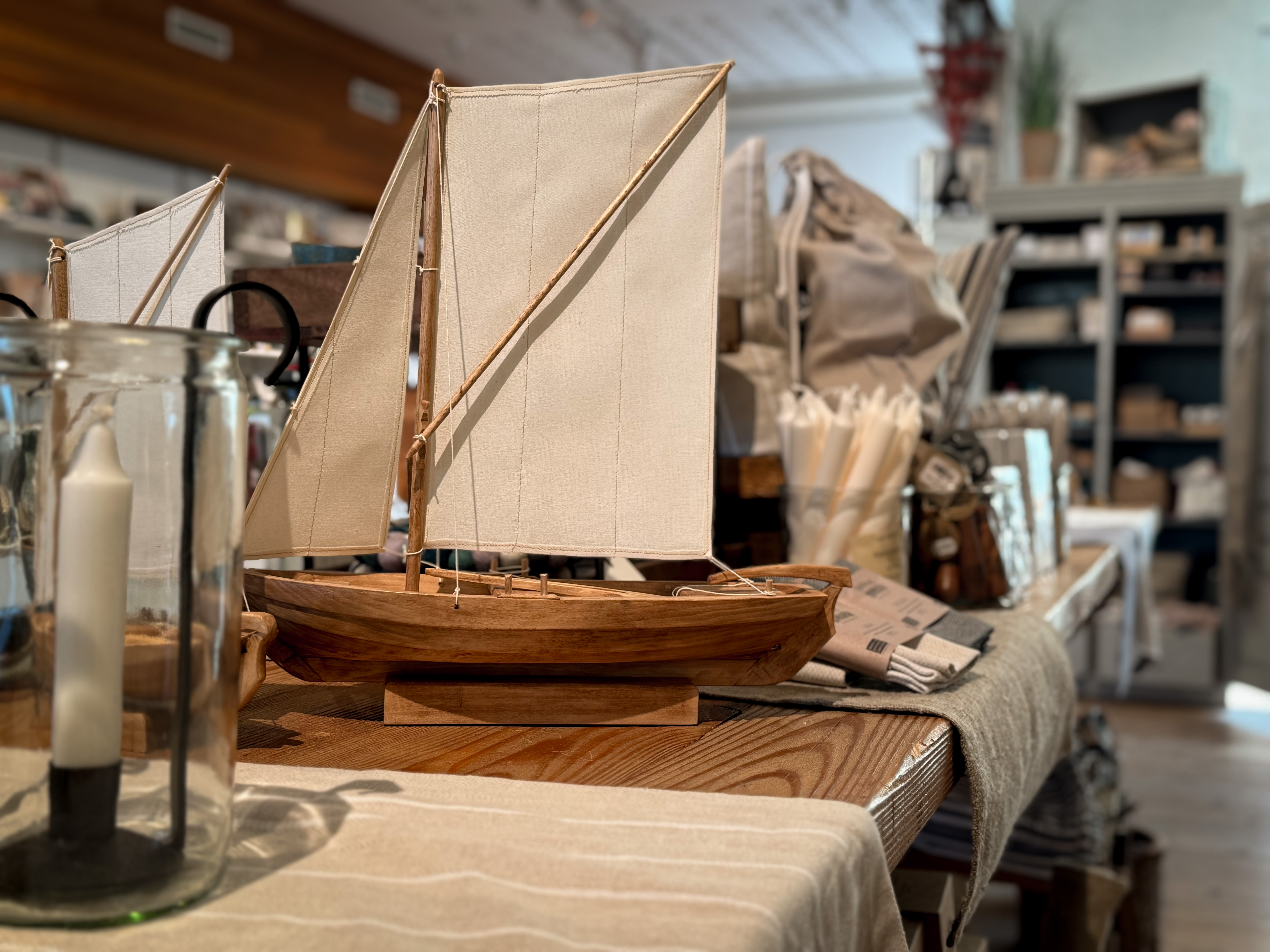 Wooden model of a sailing ship with white sails on a table in the museum shop at the Naval Museum, surrounded by nautical products and decor items.