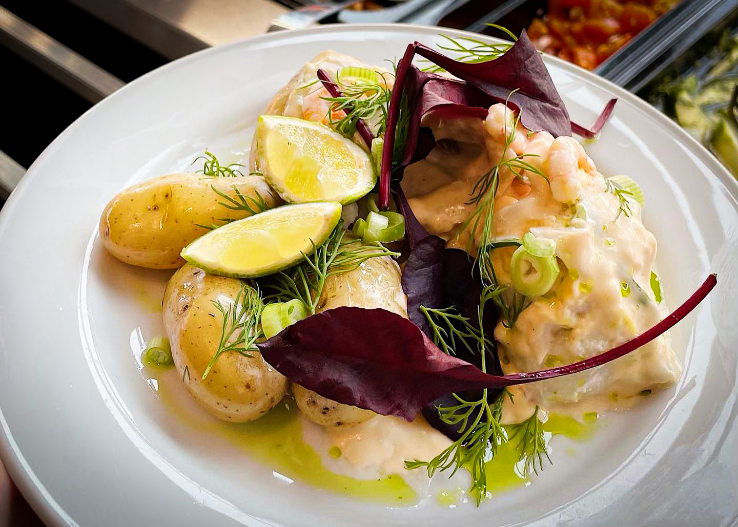 A plate of potatoes and salmon in creamy sauce, topped with shrimp, lime wedges, and fresh herbs from the restaurant at the Naval Museum.